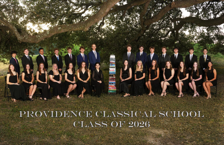 Providence Classical School Class of 2026 posed under a spreading oak tree with the many books they've read during their high school years at PCS.