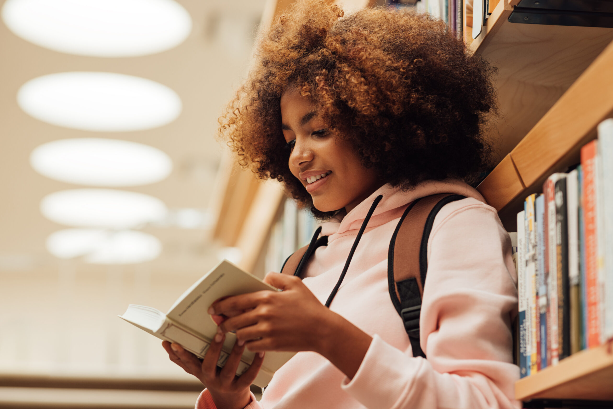 Teenage girl reading a book while standing in library.