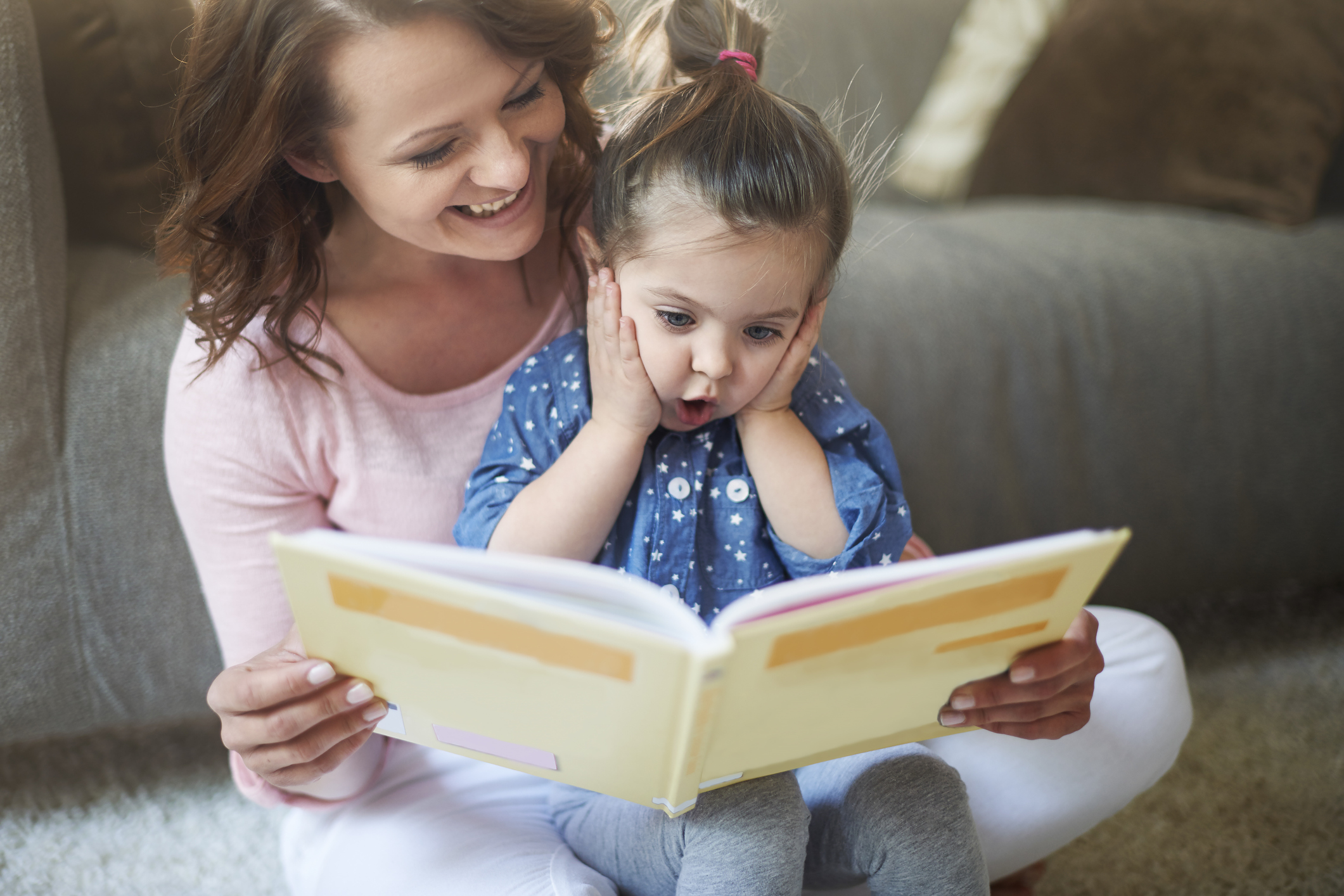 Little girl with look of surprise on her face reading with her mother