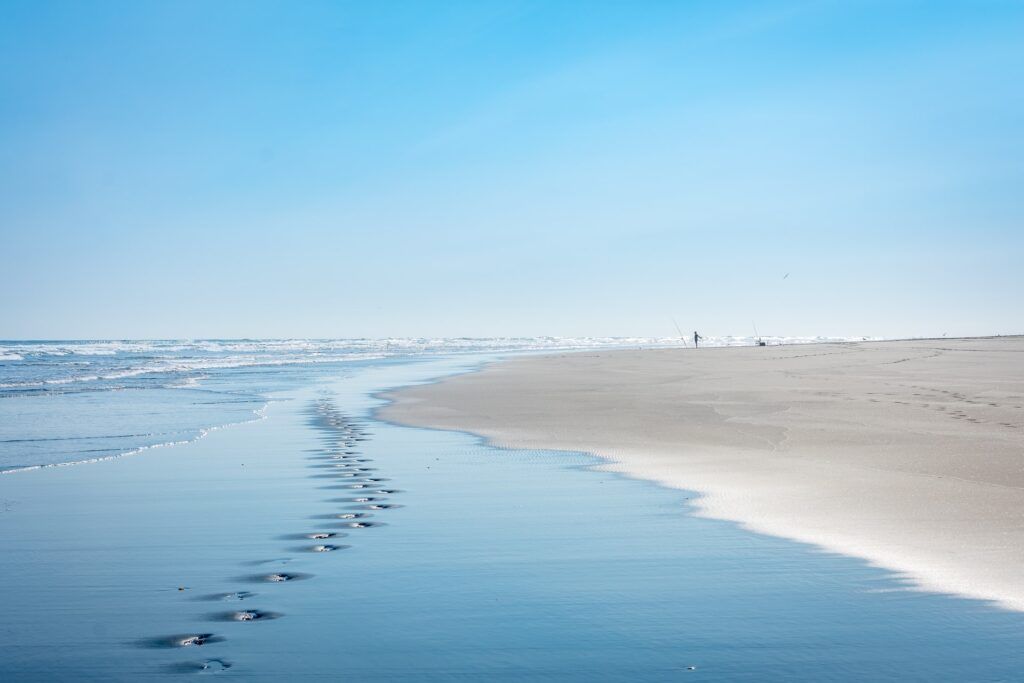 footsteps on the beach with fishermen in the distance